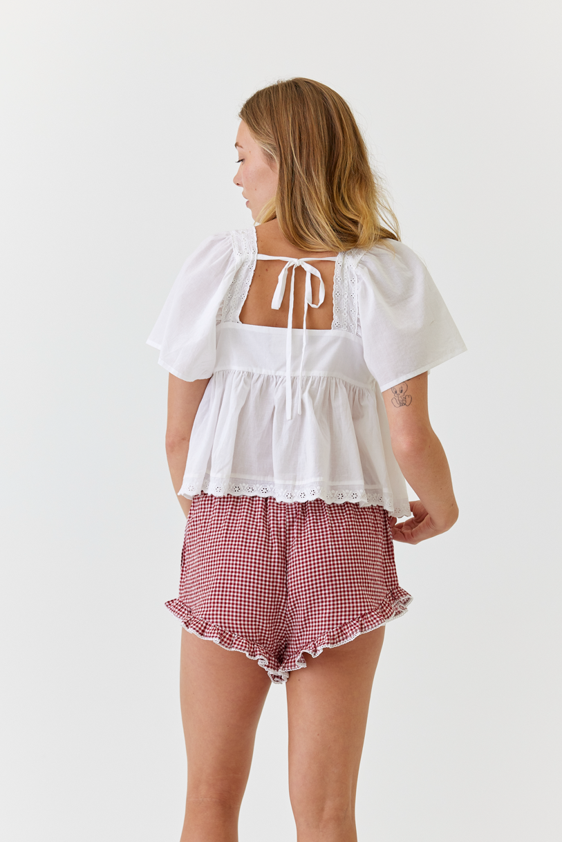 Woman wearing a white top with a lace back and red checkered shorts on a white background