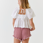 Woman wearing a white top with a lace back and red checkered shorts on a white background