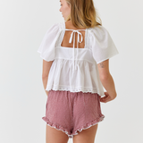 Woman wearing a white top with a lace back and red checkered shorts on a white background